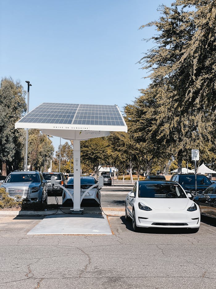 Services A white electric car charging under a solar panel in an urban setting, showcasing renewable energy use.