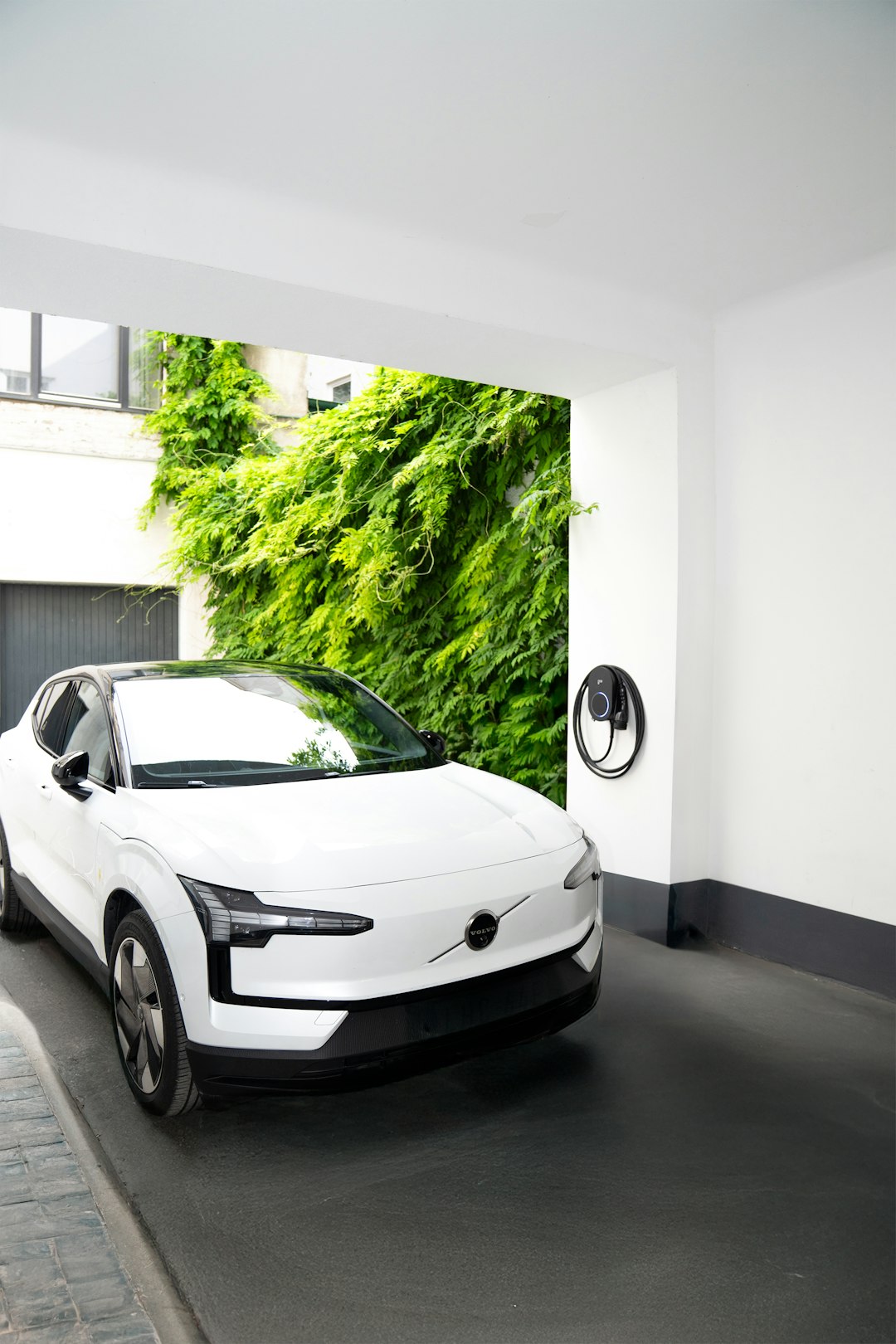 Services A white electric car sits parked in a clean, minimalist driveway beside a go-e Charger CORE mounted on a white wall